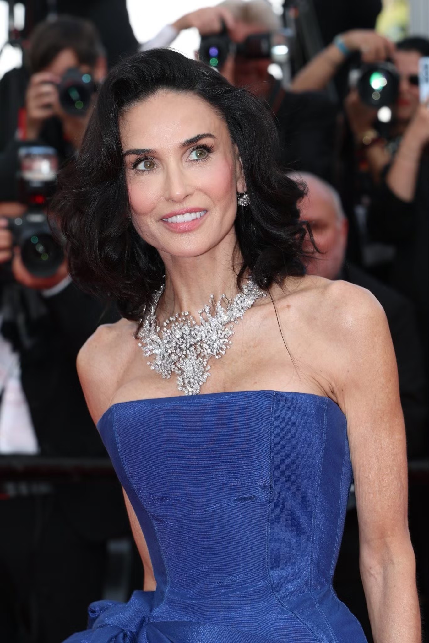 Demi Moore tiếp tục chứng minh phong độ thời trang với chiếc váy xanh dáng corset, điểm nhấn là chiếc nơ khổng lồ ở hông. Cô kết hợp cùng vòng cổ cầu kỳ và kiểu tóc bob dài uốn sóng mềm thay cho mái tóc dài quen thuộc.