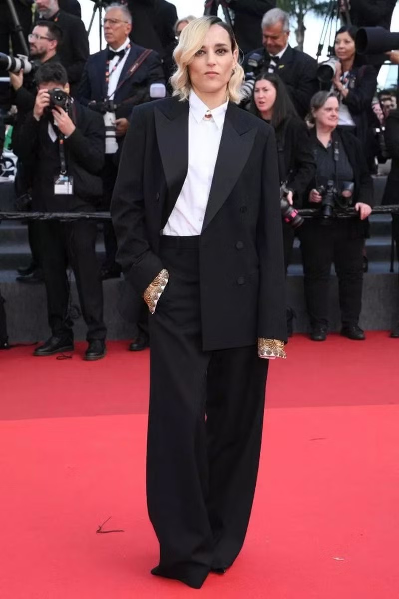 Jehnny Beth mang đến hình ảnh menswear cá tính với suit đen, sơ mi trắng cài kín cổ và ghim vàng nhỏ làm điểm nhấn. Tay áo thêu dài lộ ra khỏi blazer giúp tổng thể bớt cứng nhắc.