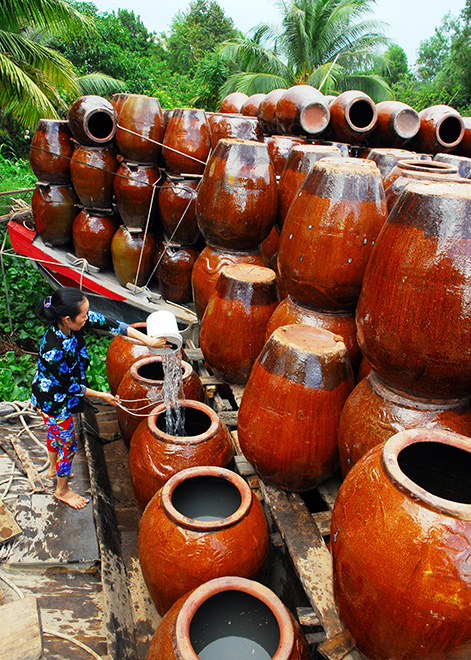 Trong ảnh là người phụ nữ đổ nước vào lu để chuẩn bị cho chuyến giao hàng bằng ghe ở miền Tây.