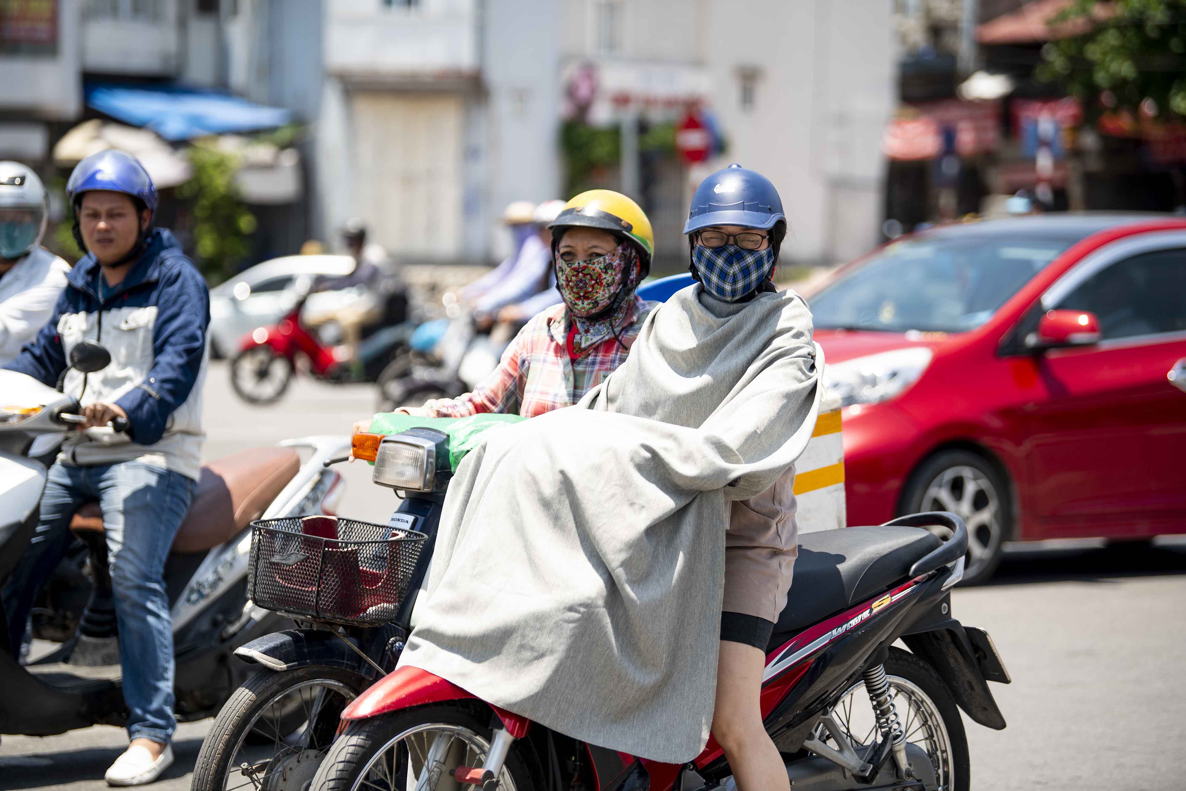 Một phụ nữ đi xe máy dùng nguyên cái chăn để chống nắng khi tham gia giao thông giữa trời nắng 38 độ