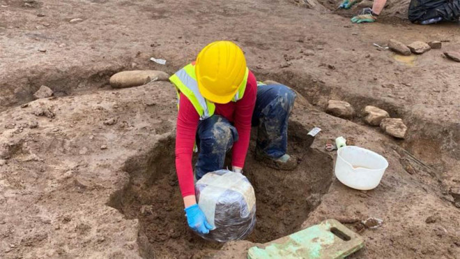 Một nhà khảo cổ đưa chiếc bình đựng hài cốt hỏa táng lên khỏi khu mộ 4.000 năm - ảnh: Fadó Archaeology