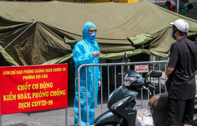 Dân quân tự vệ trong trang phục bảo hộ đang hỏi thông tin cụ thể địa điểm người nhận nhu yếu phẩm.