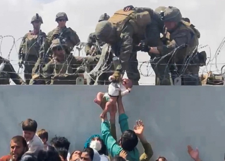 Người dân Afghanistan đưa một trẻ sơ sinh cho binh sĩ Mỹ qua tường rào ở ngoài sân bay Kabul. Ảnh: Reuters