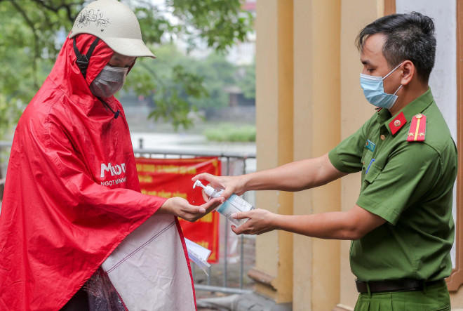 Lực lượng chức năng xịt dung dịch sát khuẩn tay cho người dân lấy đồ từ bên trong khu vực phong tỏa