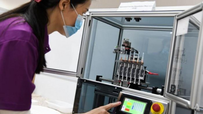Một nhân viên y tế Singapore đang thao tác trên máy phân phối vaccine tự động - ảnh CNA