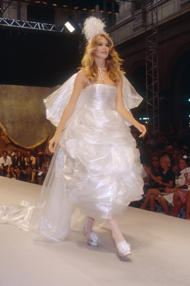 Claudia Schiffer mặc một chiếc váy cưới Chanel hình bong bóng mang tính biểu tượng với chiếc mũ đội đầu nhỏ trên sàn diễn màu xám có rèm đen. Claudia Schiffer Chanel diễn cho BST&nbsp;thời trang cao cấp Thu Đông 1991.