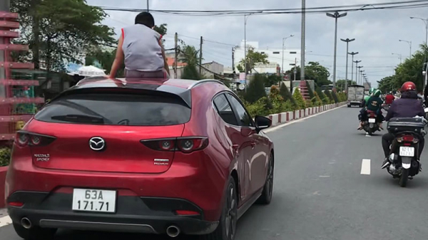 Cháu bé ngồi vắt vẻo trên mui xe trong khi chiếc xe đang lao vun vút trên đường.