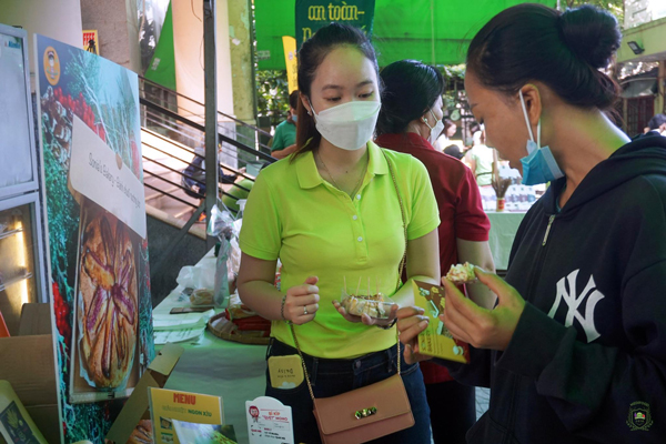 Chị đang tư vấn cho khách hàng tại hội chợ, khách hàng đang nếm thử món bánh chuối nướng bơ.