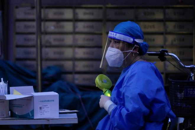 Thượng Hải vật lộn với cả sóng nhiệt
và Covid-19: Một nhân viên y tế mệt mỏi trong bộ đồ bảo hộ, cố gắng
chóng nóng bằng chiếc quạt cầm tay - Ảnh: REUTERS