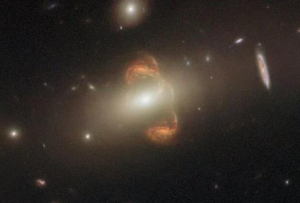 Hình ảnh độc đáo bao gồm một thiên hà màu cam và bóng ma đối xứng của nó, ở giữa là "gương thiên hà", cả 3 đều là những vật thể "xuyên không" - Ảnh: HUBBLE/NASA/ESA