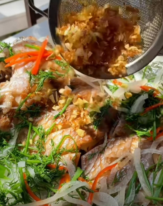Bạn trút cá từ vỉ hấp ra đĩa rồi rắc gừng, hảnh, tỏi phi lên trên mặt đĩa cá.