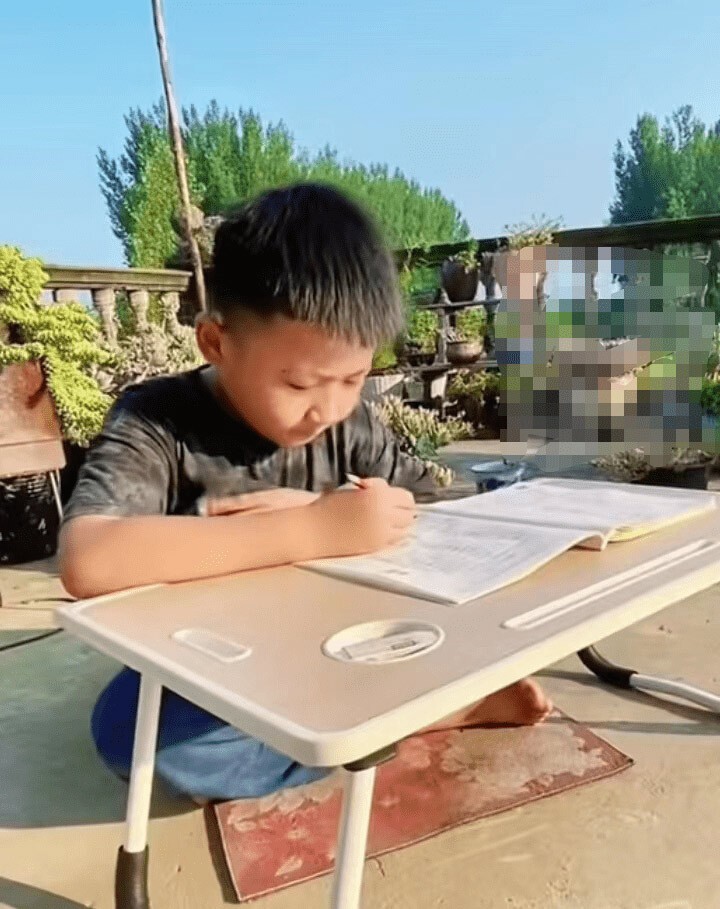 Cậu bé phải ngồi trong thời tiết nắng nóng để làm bài tập. Ảnh: Sohu
