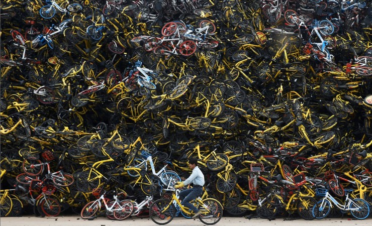 Một người đi xe đạp qua một núi xe đạp chia sẻ không sử dụng tới tại Hạ Môn, Phúc Kiến, Trung Quốc. 
