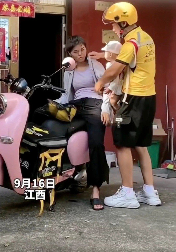 Wuzi đang địu con trai trước ngực rồi đội mũ bảo hiểm cho vợ trước khi cả 3 cùng đi làm. Ảnh: Weibo.&nbsp;