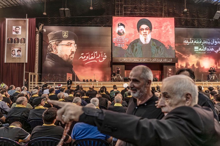 Lãnh đạo Hezbollah Hassan Nasrallah xuất hiện trên màn hình lớn ở Beirut, Lebanon phát biểu về mong muốn trả thù cho cái chết của Fuad Shukr (bên trái). Ảnh: WSJ.