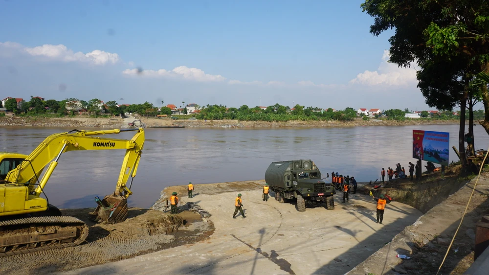 Trong ảnh là đường dẫn xuống cầu phao phía bờ Tam Nông đi chéo góc rồi rẽ xuống sông. Đối diện bên kia là phía xã Phùng Nguyên, huyện Lâm Thao, với đường dẫn dốc đi thẳng, vuông góc xuống sông Hồng. Trong quá trình thi công, hàng trăm khối đã kích thước lớn đã được đổ xuống hai đầu dốc, để tạo móng, chống sạt lở hai đầu cầu phao. Tuy nhiên, dốc phía bên Lâm Thao những ngày qua vẫn bị hư hỏng, nên máy xúc đang tiếp tục gia cố để chuẩn bị đổ bê tông hoàn thiện. Ảnh: XUÂN NGUYỄN