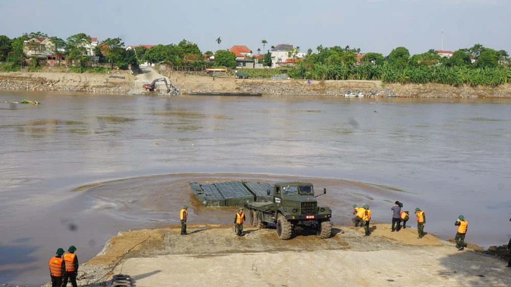 Vị trí cầu phao nằm cách cầu Phong Châu đã bị sập khoảng 400m xuôi về phía hạ lưu. Những ngày qua, lực lượng công binh đã san lấp mặt bằng, rải đá, đổ bê tông để tạo ra một dốc thoải xuống dưới mặt nước. Ảnh: XUÂN NGUYỄN