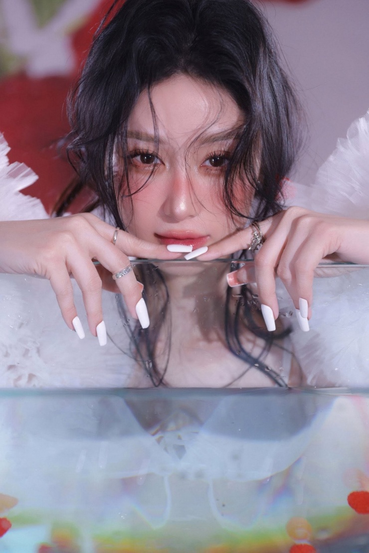 Gương mặt được trang điểm nhẹ nhàng với tông màu tươi sáng, đôi môi được tô điểm bằng màu son đỏ cherry ngọt ngào, vừa tạo điểm nhấn vừa giữ được nét thanh tú, trong trẻo. Phụ kiện đi kèm cũng được lựa chọn tỉ mỉ, như chiếc kẹp tóc hình quả mâm xôi nhỏ xinh, càng làm tăng thêm sự đáng yêu và tinh nghịch.