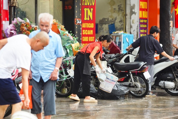 Người dân sống tại mặt phố đường Nguyễn Trãi tát nước, quét rác, bùn sau khi nước tràn vào nhà.