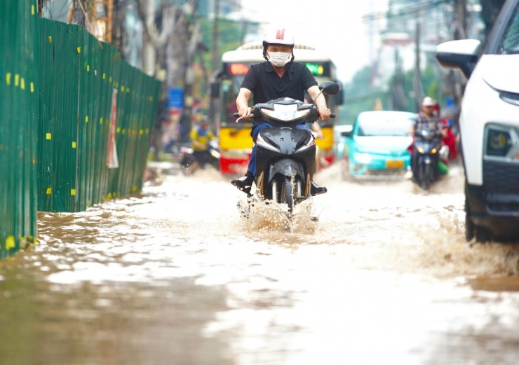 Người điều khiển xe máy co chân băng qua phố ngập nước.