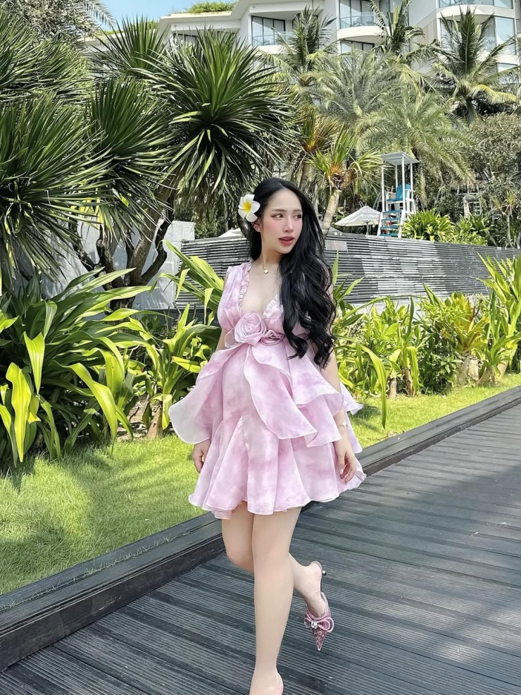 Dù bụng bầu vượt mặt nhưng Joyce Phạm vẫn tự tin mang giày cao gót để thấp với màu hồng cùng tone với váy. Cô cũng khéo léo kết hợp phụ kiện đậm tính nhiệt đới như bông hoa sứ cài tóc.
