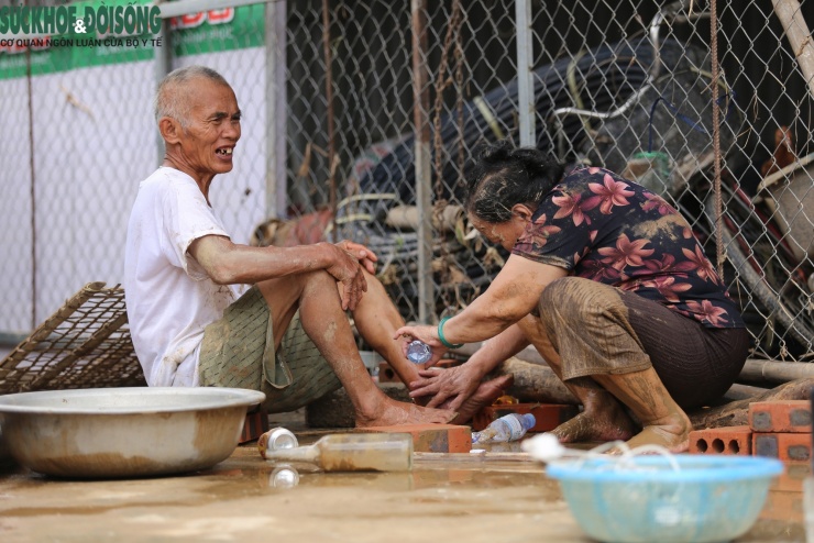 Cụ bà lấm len bùn đất rửa lại vết thương cho cụ ông.