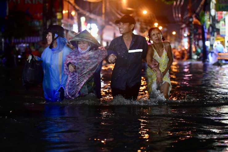 Bà Phạm Thị Công (58 tuổi, áo vàng) nhờ người dìu qua đường ngập. "Nhà tôi gần đây mà nước chảy xiết tôi không dám đi", bà nói.