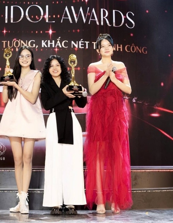 Trên sân khấu, người đẹp tỏa sáng với bộ đầm đỏ trễ vai xếp bèo cùng kiểu tóc búi cao. Chất liệu voan mềm tạo độ rủ giúp bộ cánh trở nên gọn gàng, không bị cồng kềnh so với nhiều bộ đầm có cấu trúc tương tự. Kiểu tóc búi cao và sandals màu nude tạo sự thanh thoát cho gương mặt, cổ và chân.