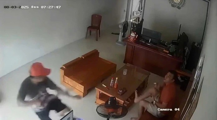 Camera ghi lại hình ảnh người đàn ông mũ đỏ xông vào nhà chém đứt cánh tay người ngồi ghế. (Ảnh cắt từ clip)
