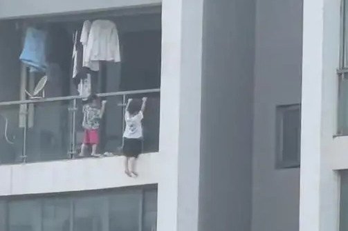 Hai đứa trẻ leo ra ngoài lan can ban công chơi khiến nhiều người thót tim. Ảnh: Sohu