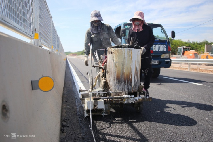 Công tác thi công trên tuyến cao tốc Vạn Ninh - Cam Lộ đang diễn ra khẩn trương. Các điểm cắt ngang để phương tiện qua lại đã được trải nhựa và công nhân đang sơn vạch kẻ đường dưới thời tiết nắng nóng gần 37 độ C. Các hạng mục an toàn giao thông như lan can, hộ lan và biển báo đã được lắp đặt hoàn chỉnh trên toàn tuyến.