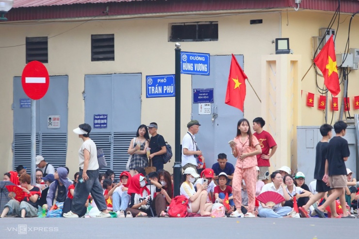 Người dân "xí chỗ" vỉa hè góc đường Hùng Vương - Trần Phú, gần quảng trường Ba Đình. Họ mang theo áo mưa, chiếu, nước, đồ ăn để chờ đến tối đoàn diễu binh đi qua. Hà Nội một tuần nay mưa nắng thất thường. Ảnh: Phạm Dự