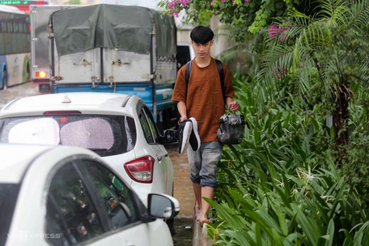 Thanh niên bỏ giày, lội bộ trên vỉa hè quốc lộ 6 để tránh ngập. Ảnh: Gia Chính