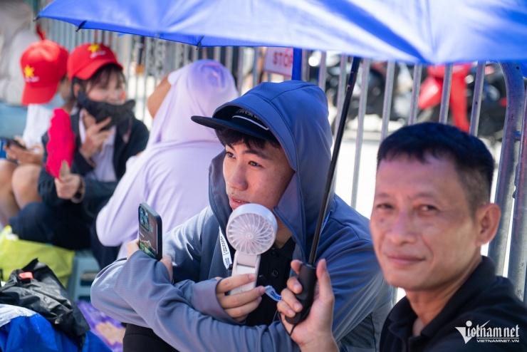 Nhiệt độ ngoài trời lúc này khoảng 30 độ C rất oi nóng, nhiều gia đình "chia ca" thay phiên nhau ra ngồi giữ chỗ. Quạt cầm tay, áo chống nắng, ô dù là thứ không thể thiếu.