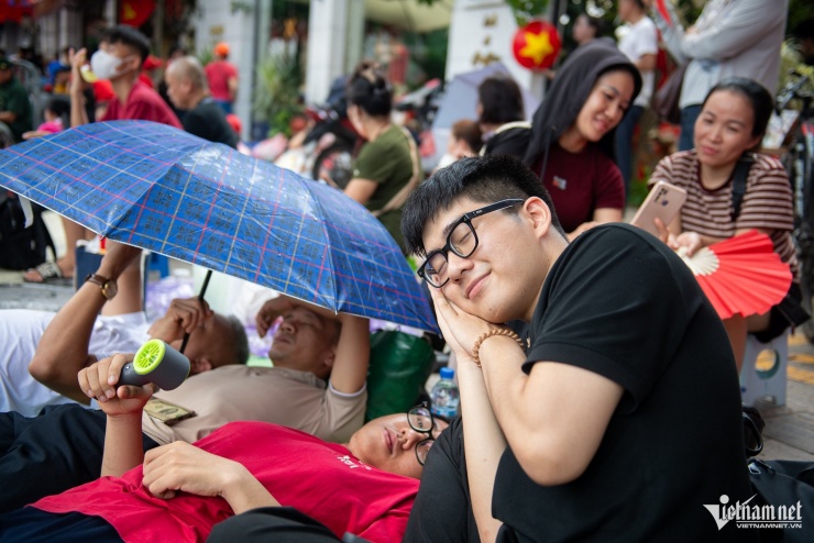 Gia đình anh Tuấn tranh thủ che ô, ngả lưng nghỉ trưa trên vỉa hè. 