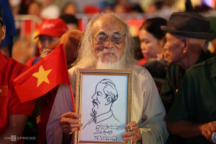 Cụ Nguyễn Văn Cần 86 tuổi, mang theo cờ đỏ sao vàng và bức tranh vẽ chủ tịch Hồ Chí Minh mà ông được, cổ vũ lực lượng diễu binh trong đêm. Ảnh: Quỳnh Trần