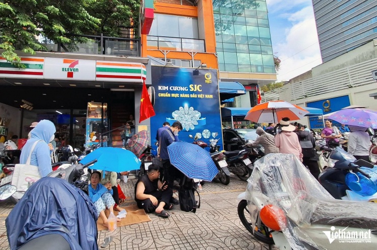 Khách hàng trải bạt trên vỉa hè, cầm ô chờ đến lượt mua vàng. Có người cho hay đã phải xếp hàng mua vàng từ 10h tối hôm trước. Ảnh: Trần Chung