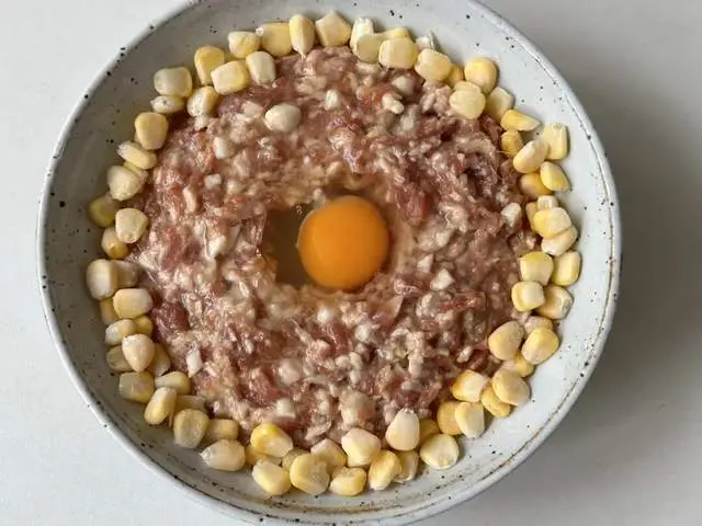 Cho phần thịt đã trộn vào bát, dàn phẳng bề mặt, khoét một lỗ nhỏ giữa bát rồi đập trứng gà cho vào. Xung quanh có thể rắc thêm hạt ngô hoặc đậu nành tươi cho đẹp mắt.