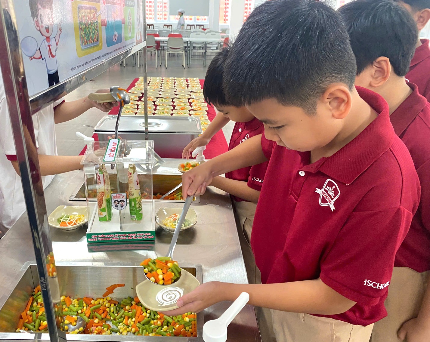 Các em học sinh hứng khởi tự gắp thực phẩm ở quầy buffet rau trong giờ ăn trưa.