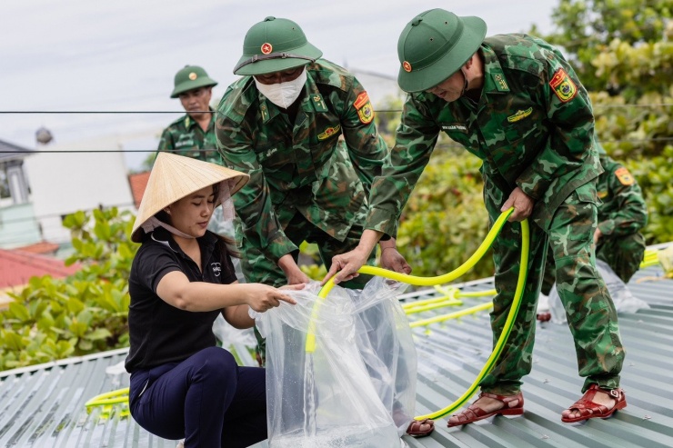 Bộ đội cùng giáo viên bơm nước vào các bao bóng đặt lên mái nhà nhằm chống tốc mái - một sáng kiến khá hiệu quả của người dân làng biển những năm gần đây.