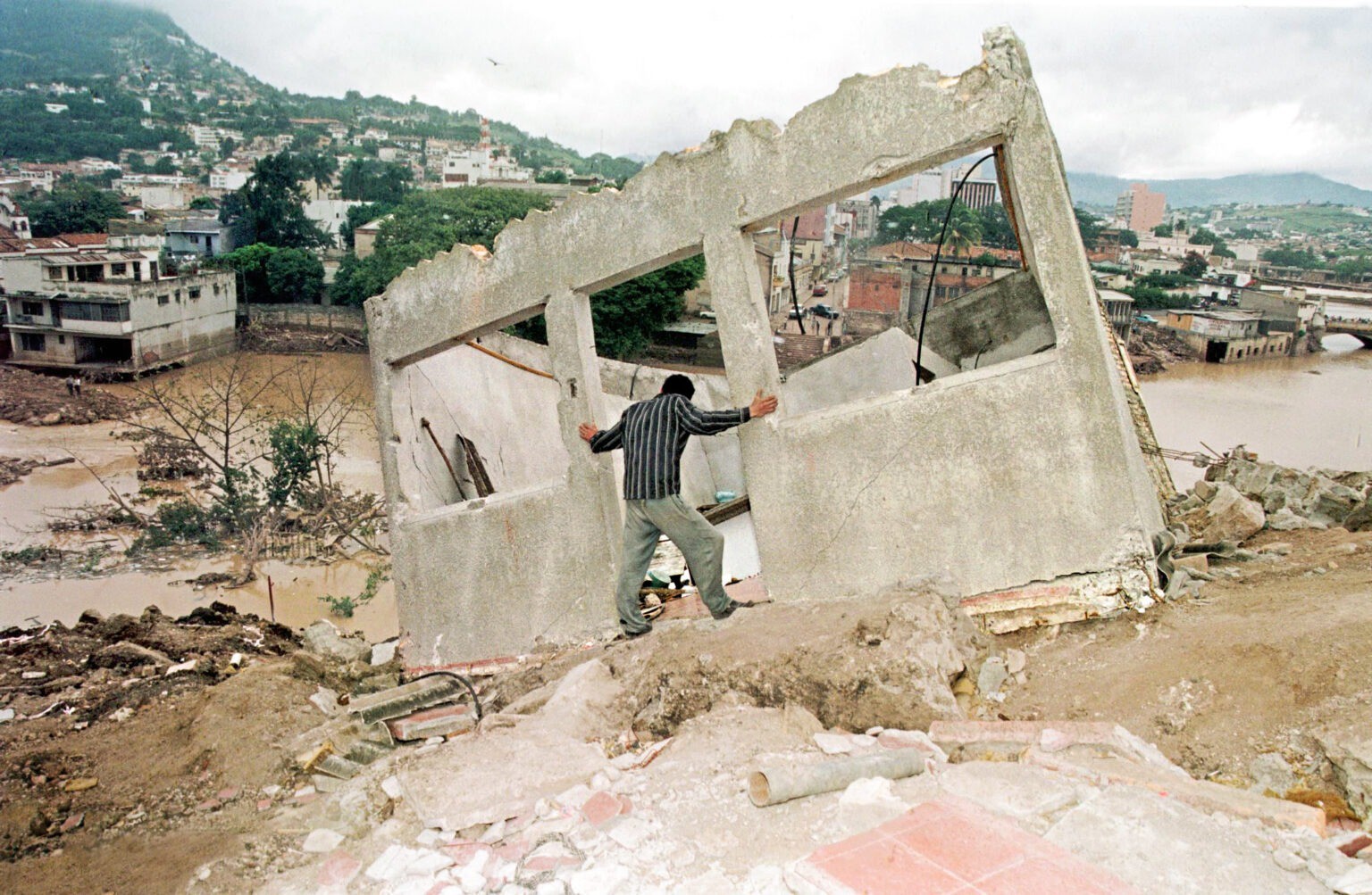 Một người đàn ông đứng cạnh ngôi nhà bị tàn phá trong siêu bão Mitch ở Honduras. Ảnh: AFP