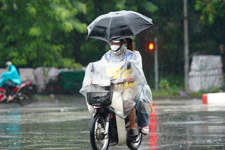 Người đi xe máy vừa dùng áo mưa, vừa dùng ô để vượt qua mưa lớn.