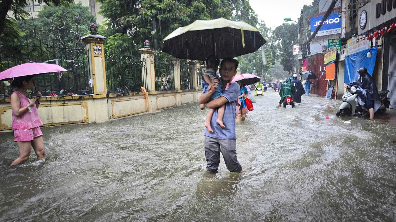 Nước ngập sâu, người dân và học sinh giờ tan tầm đi lại khó khăn. Nhiều phụ huynh bì bõm 'dò dẫm' băng qua biển nước để đón con về nhà.