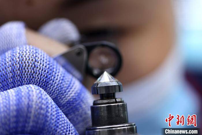 Công nhân dùng kính lúp soi kim cương đang mài. Ảnh: China News