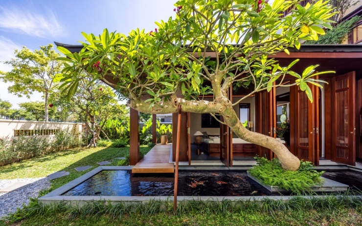 Thay vì tăng diện tích xây dựng, nhóm thiết kế dành khoảng lùi phía trước làm sân vườn, bố trí cây xanh và mặt nước. Khoảng trống tạo lớp đệm giữa đường phố và không gian ở, đồng thời hỗ trợ thông gió, lấy sáng và hạn chế bức xạ nhiệt. Hệ mái và cửa được thiết kế nhằm tái hiện tinh thần kiến trúc truyền thống. Mái và mái hiên rộng vừa tạo hình cho công trình, vừa hạn chế tác động trực tiếp của nắng, mưa vào bên trong. Hệ cửa lớn có thể mở hoàn toàn, vừa đảm bảo riêng tư, vừa thu hẹp ranh giới trong - ngoài và tăng kết nối với thiên nhiên.