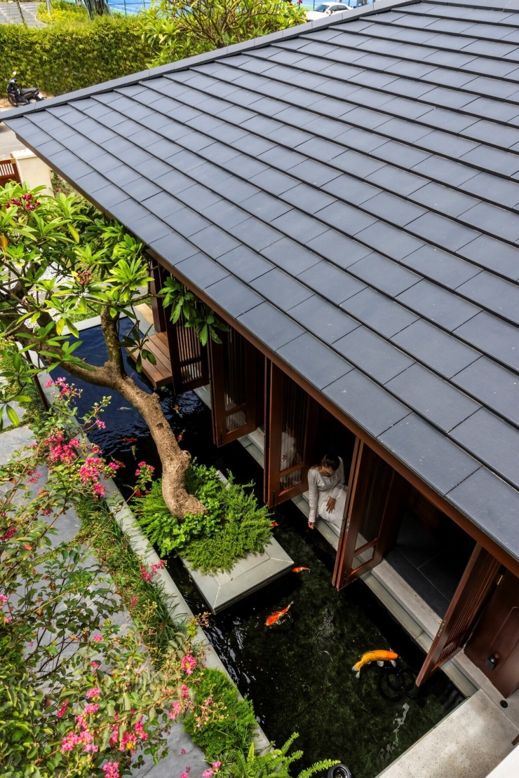 Hồ cá chạy sát khối phòng khách, kết hợp các lớp cây thấp và cây thân gỗ.