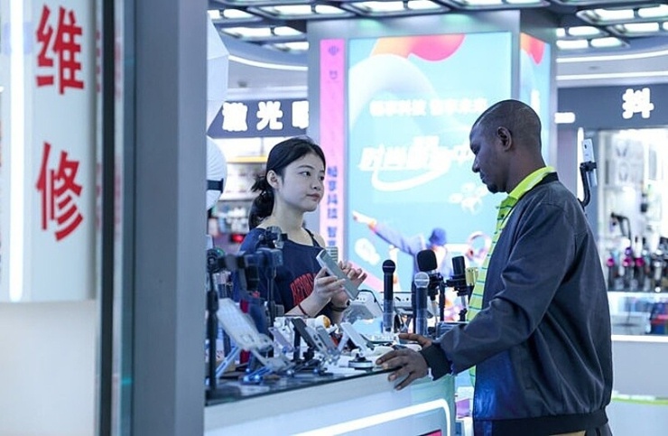 Chủ một quầy hàng trong chợ điện tử Hoa Cường Bắc đang giới thiệu sản phẩm cho một khách nước ngoài hôm 22/7/2025. Ảnh: Xinhua