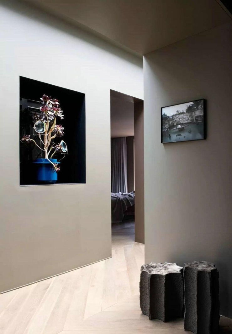 Hành lang dẫn vào phòng ngủ dùng gam màu đồng nhất với khu vực nghỉ ngơi trên tầng hai. Sàn gỗ sáng màu lát xương cá giúp kéo dài hướng nhìn. Tranh treo tường và cặp ghế đôn có bề mặt thô tạo điểm nhấn trên nền tường trung tính.