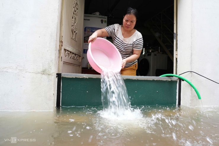 Cùng lúc, chị Trần Thị Hồng ở ngõ 39 Tứ Liên cũng đang tát từng chậu nước. Người phụ nữ đã dùng tấm thép cao 60 cm chắn trước cửa những nước vẫn tràn, chị phải cắm nhờ điện nhà hàng xóm để bơm nước khỏi nhà. Ảnh: Huy Mạnh