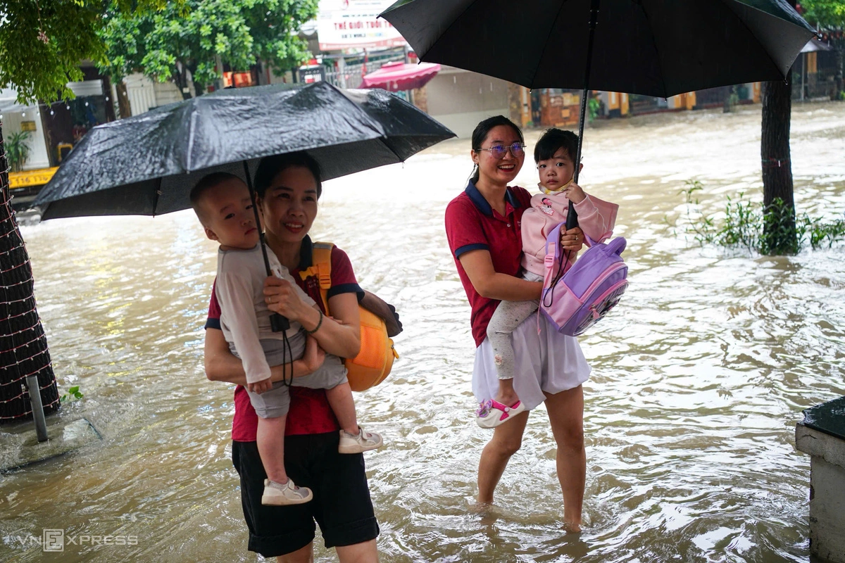 Chị Thu Huyền và Thu Phương, giáo viên trường mầm non ở Khu đô thị Nam An Khánh đội mưa, đón học sinh đến lớp. Ảnh: Hoàng Giang